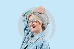 Happy beautiful girl in fashionable jeans jacket and hat on blue background.