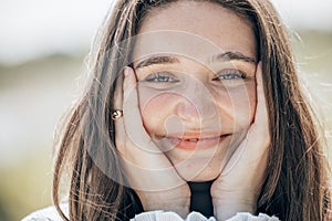 Happy beautiful girl holding her cheeks with a laugh, looking at the camera. Pretty young woman clean fresh skin