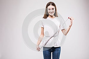 Happy and beautiful girl measuring her waist fitness with a ruler over grey background. Health concept