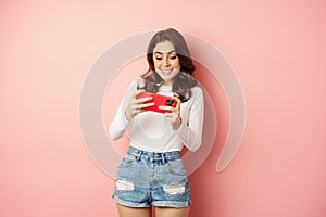 Happy beautiful girl playing mobile video game, holding smartphone horizontally, watching on cellphone with excited face