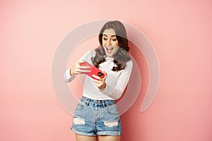 Happy beautiful girl playing mobile video game, holding smartphone horizontally, watching on cellphone with excited face