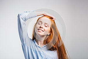 Happy beautiful girl smiling with closed eyes touching her red hair