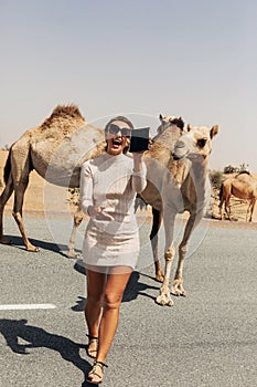 A happy beautiful girl, smiling, takes a selfie with a camel by the road during a trip to the desert, Dubai, UAE