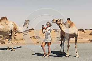 A happy beautiful girl, smiling, takes a selfie with a camel by the road during a trip to the desert, Dubai, UAE