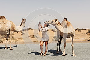 A happy beautiful girl, smiling, takes a selfie with a camel by the road during a trip to the desert, Dubai, UAE