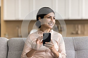 Happy beautiful Indian woman holding mobile phone, looking away