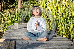 Happy beautiful kid doing yoga bare feet sitting on wood