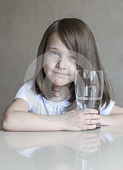 Happy beautiful little girl drinking clear water. Portrait of smiling baby holding transparent glass