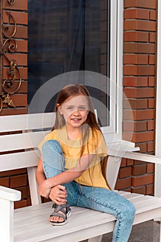 happy beautiful little girl with long blonde hair wearing casual clothes sitting on a bench