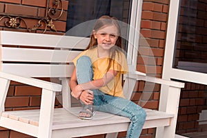 happy beautiful little girl with long blonde hair wearing casual clothes sitting on a bench