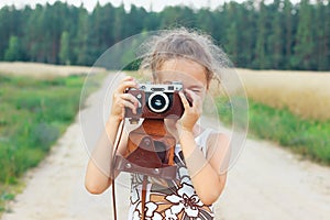 Happy beautiful  little girl in retro outfit  is taking pictures with old film camera