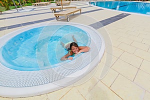 Happy beautiful little girl swimming and relaxing in small Jacuzzi near the pool