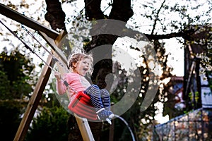 Happy beautiful little toddler girl having fun on swing in domestic garden. Cute healthy child swinging under blooming