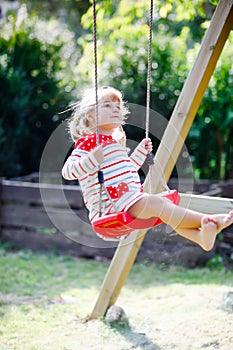 Happy beautiful little toddler girl having fun on swing in domestic garden. Cute healthy child swinging under blooming