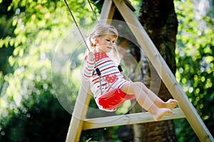 Happy beautiful little toddler girl having fun on swing in domestic garden. Cute healthy child swinging under blooming