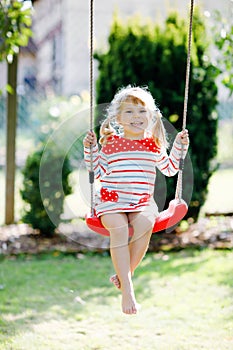 Happy beautiful little toddler girl having fun on swing in domestic garden. Cute healthy child swinging under blooming