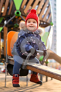 Happy beautiful little toddler girl having fun on swing in the playground. Baby smiles and laughing.