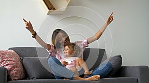 Happy beautiful loving family young mother and daughter laughing sitting on the couch, smiling mom with child having fun enjoy con