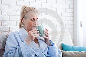 Happy beautiful middle aged woman drinking coffee on sofa at home