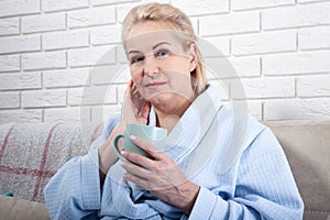 Happy beautiful middle aged woman drinking coffee on sofa at home