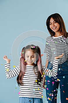 Happy beautiful mom and daughter playing with confetti. Over blue background.