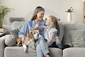 Happy beautiful mother embracing kid and touching dog on sofa