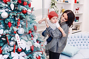 Happy beautiful mother having fun with her infant son near Christmas Tree in Christmas evening.