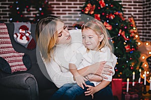 Happy beautiful mother and her little daughter posing near Christmas tree in a holiday interior