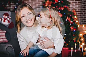 Happy beautiful mother and her little daughter posing near Christmas tree in a holiday interior