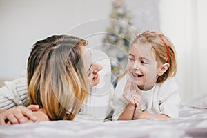 Happy beautiful mother and her little daughter posing near Christmas tree in a holiday interior