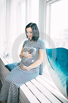 Happy beautiful pregnant caucasian woman with big belly in dress in the child room with balloons, future parrents