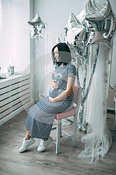 Happy beautiful pregnant caucasian woman with big belly in dress in the child room with balloons, future parrents