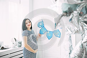 Happy beautiful pregnant caucasian woman with big belly in dress in the child room with balloons, future parrents