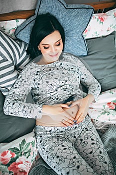 Happy beautiful pregnant caucasian woman with big belly in pajamas in the bedroom, future parrents, waiting for a child