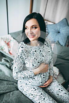 Happy beautiful pregnant caucasian woman with big belly in pajamas in the bedroom, future parrents, waiting for a child