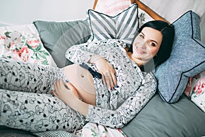 Happy beautiful pregnant caucasian woman with big belly in pajamas in the bedroom, future parrents, waiting for a child