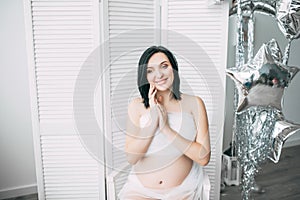 Happy beautiful pregnant caucasian woman with big belly in white underwear in the bedroom, future parrents, waiting for