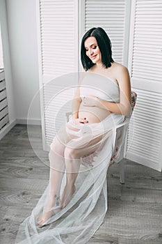 Happy beautiful pregnant caucasian woman with big belly in white underwear in the bedroom, future parrents, waiting for