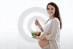 Happy beautiful pregnant woman holding bowl with fresh vegetable salad
