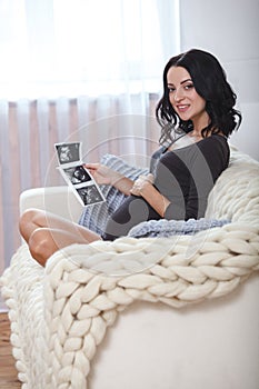 Happy beautiful pregnant woman relaxing on sofa with echo in hands