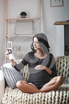 Happy beautiful pregnant woman relaxing on sofa with echo in hands