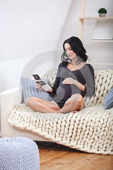 Happy beautiful pregnant woman relaxing on sofa with echo in hands