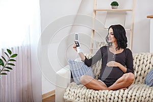 Happy beautiful pregnant woman relaxing on sofa with echo in hands