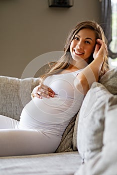 Happy beautiful pregnant woman sitting in sofa touching her belly
