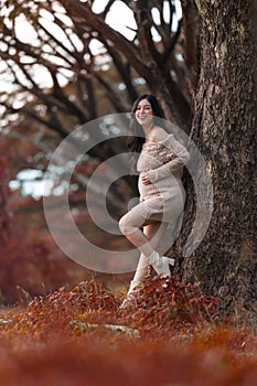 Happy beautiful pregnant woman stroking her belly in the autumn park