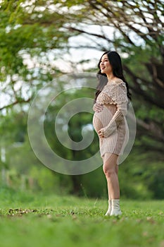 Happy beautiful pregnant woman stroking her belly in the park