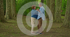 Happy beautiful senior couple dancing in autumn park. Full length portrait of cheerful active retired man and woman