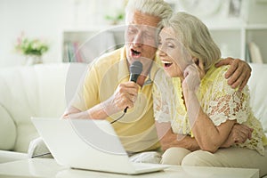 Happy beautiful senior couple singing karaoke with laptop at home