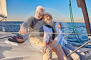 Happy beautiful senior family couple hugging and smiling while relaxing on a sail boat or yacht deck floating in a calm