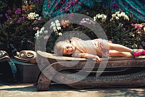 Happy beautiful smiling child girl lying on bench in blossoming flower garden with orchids concept childhood lifestyle